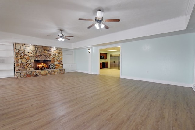 unfurnished living room with built in shelves, a textured ceiling, ceiling fan, a fireplace, and light hardwood / wood-style floors