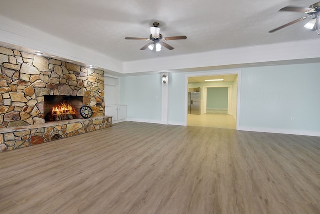 unfurnished living room featuring a stone fireplace, ceiling fan, wood-type flooring, and a textured ceiling