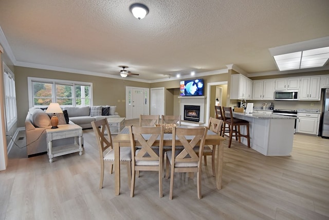 dining room featuring a textured ceiling, ceiling fan, light wood-type flooring, and crown molding