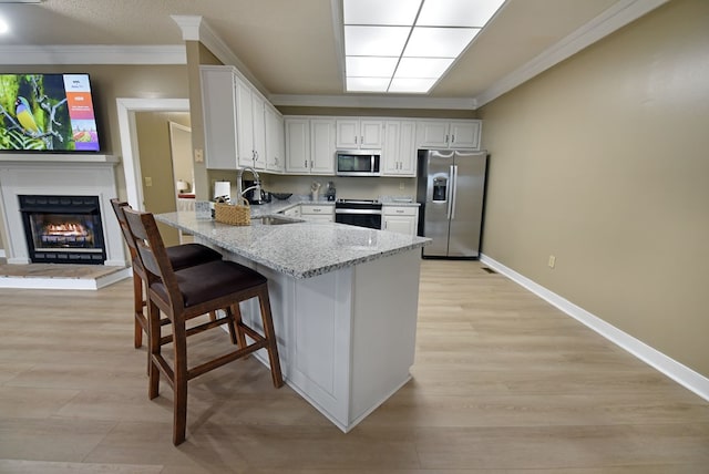 kitchen with sink, a kitchen breakfast bar, light stone counters, white cabinets, and appliances with stainless steel finishes