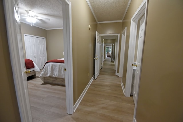 hallway featuring light hardwood / wood-style floors, ornamental molding, and a textured ceiling