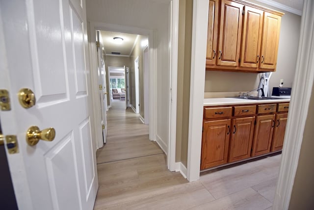 corridor featuring light wood-type flooring, ornamental molding, and sink