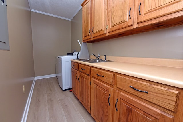 clothes washing area with cabinets, sink, crown molding, washing machine and dryer, and light wood-type flooring