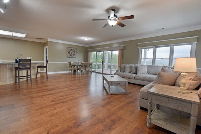 living room featuring wood-type flooring, a textured ceiling, ceiling fan, and crown molding