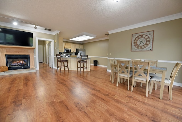 dining room with light wood-type flooring, a textured ceiling, rail lighting, and crown molding