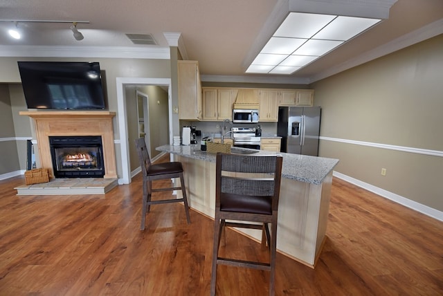 kitchen featuring a breakfast bar area, dark wood-type flooring, ornamental molding, and appliances with stainless steel finishes