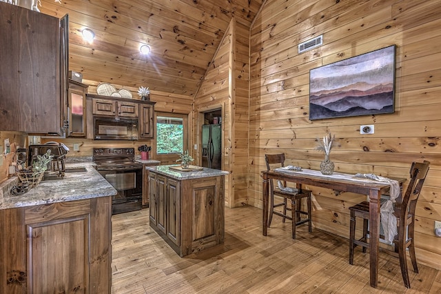 kitchen with light stone countertops, wooden walls, black appliances, light hardwood / wood-style flooring, and a kitchen island