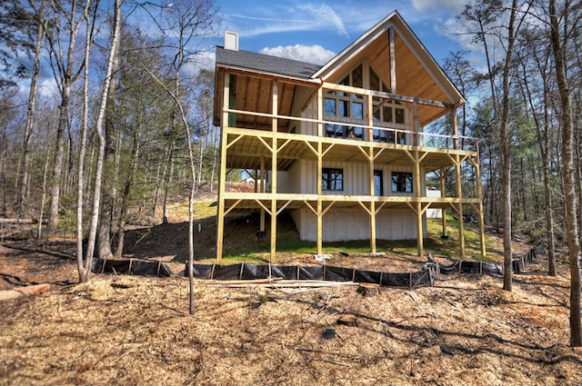 back of house featuring roof with shingles, a wooden deck, a balcony, and a chimney