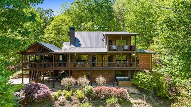 back of house featuring metal roof, stairway, a wooden deck, a chimney, and a hot tub