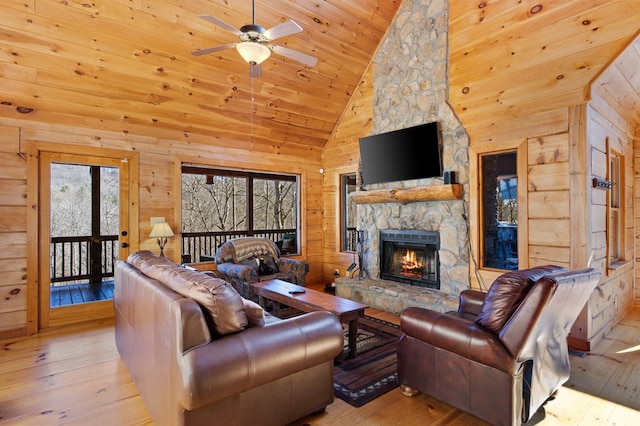 living room featuring high vaulted ceiling, a fireplace, wooden walls, and light hardwood / wood-style flooring