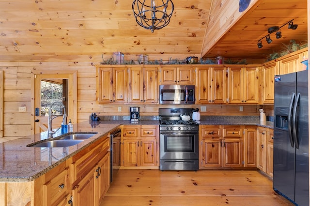 kitchen with black appliances, light wood-type flooring, decorative light fixtures, wood walls, and sink