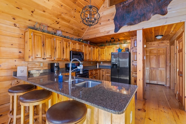 kitchen featuring light hardwood / wood-style floors, black appliances, kitchen peninsula, lofted ceiling, and wooden walls