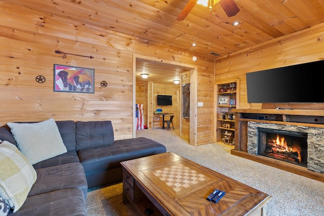 carpeted living area with a stone fireplace, wood walls, wood ceiling, and a ceiling fan