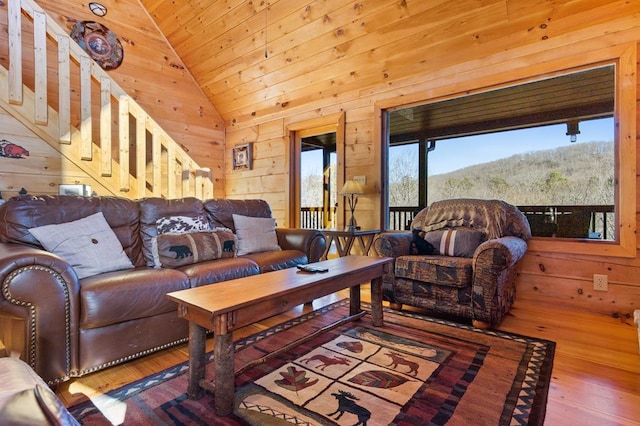 living room with vaulted ceiling, wooden walls, wood finished floors, wooden ceiling, and a forest view