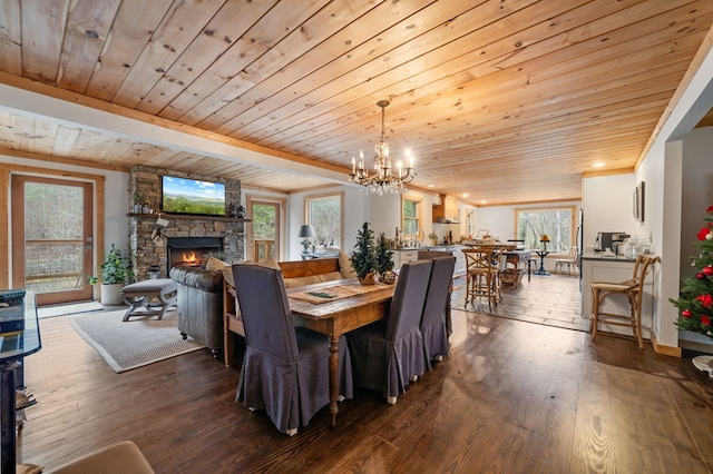 dining area with wooden ceiling, hardwood / wood-style floors, a stone fireplace, and an inviting chandelier