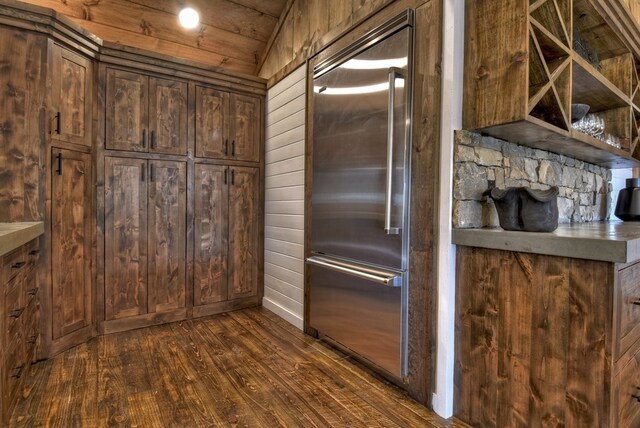 kitchen featuring dark wood-type flooring, wooden walls, lofted ceiling, and built in fridge