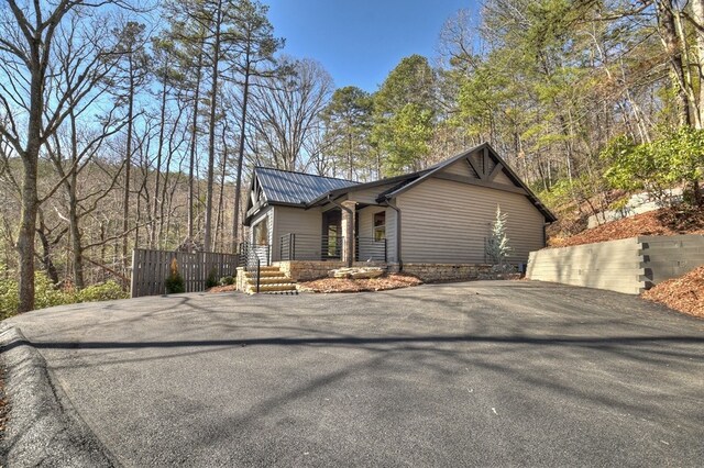 view of property exterior featuring fence, metal roof, stone siding, and aphalt driveway