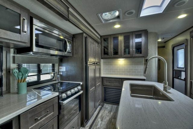 kitchen with a skylight, light stone counters, stainless steel appliances, sink, and light hardwood / wood-style floors