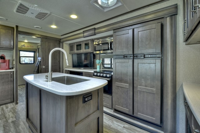 kitchen featuring light wood-type flooring, oven, a kitchen island with sink, and sink