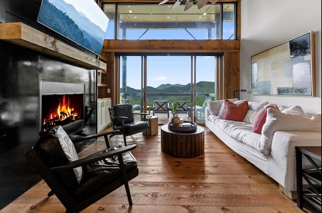 living area with a lit fireplace, a high ceiling, a mountain view, and wood finished floors