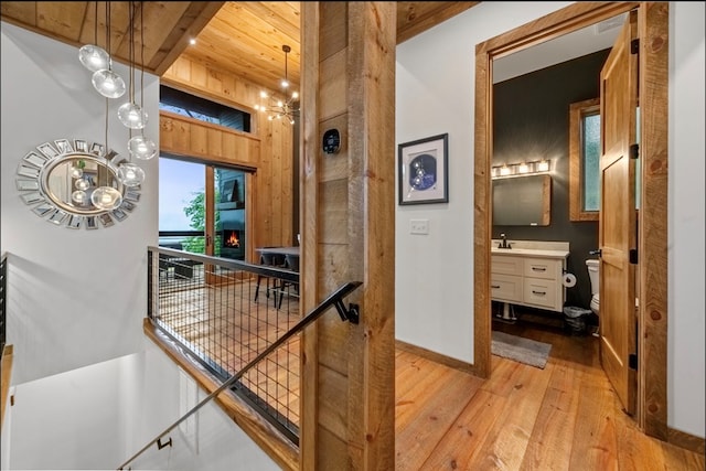 hallway featuring baseboards, wood ceiling, light wood-style flooring, beamed ceiling, and a sink