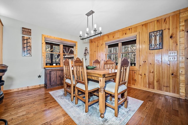 dining room featuring wooden walls, an inviting chandelier, and dark wood-type flooring