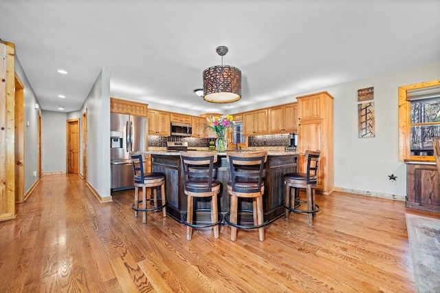 kitchen featuring a center island, hanging light fixtures, stainless steel appliances, light hardwood / wood-style floors, and tasteful backsplash