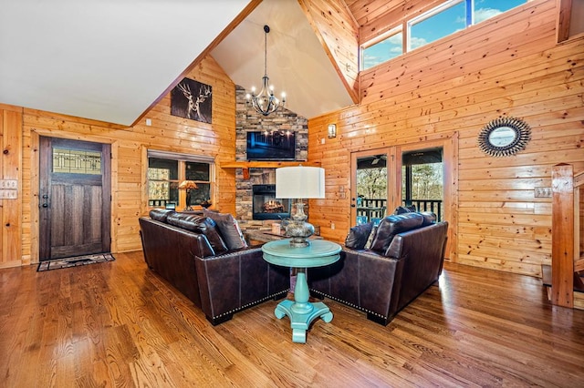 living room with wood walls, hardwood / wood-style floors, an inviting chandelier, high vaulted ceiling, and a stone fireplace