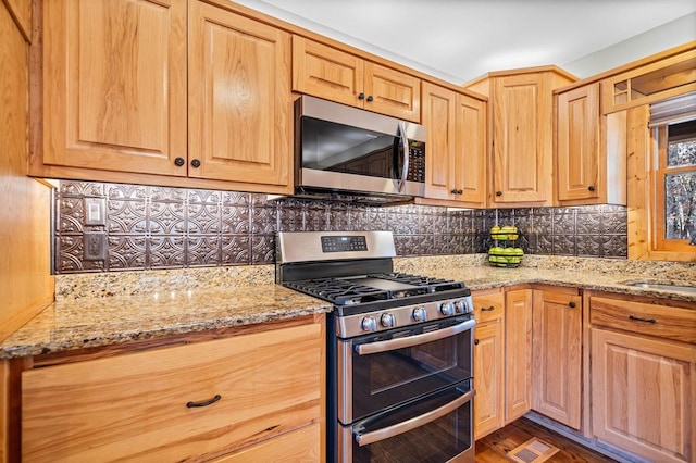 kitchen featuring sink, appliances with stainless steel finishes, light stone counters, backsplash, and dark wood-type flooring