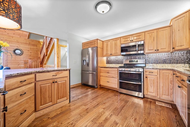 kitchen with appliances with stainless steel finishes, light wood-type flooring, light brown cabinetry, and light stone countertops