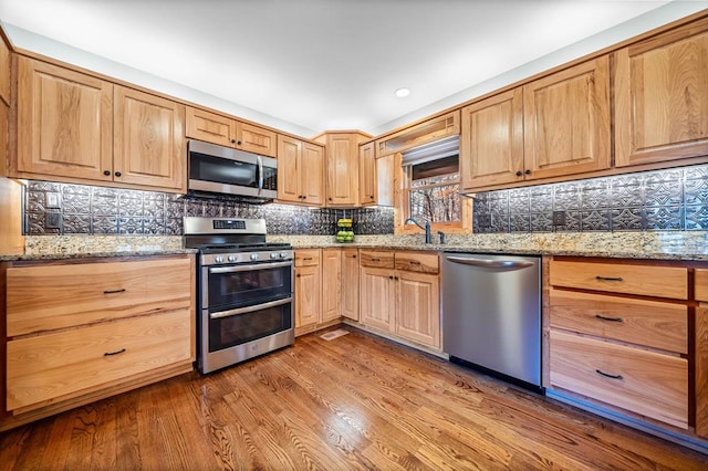 kitchen featuring light stone counters, light hardwood / wood-style flooring, decorative backsplash, appliances with stainless steel finishes, and sink