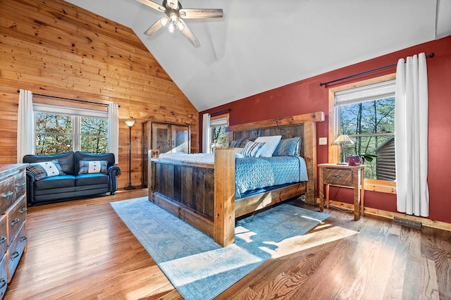 bedroom featuring ceiling fan, light hardwood / wood-style floors, wooden walls, and lofted ceiling