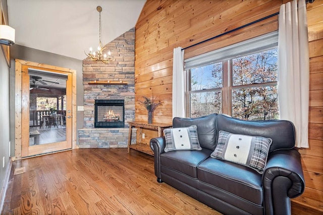 living room with hardwood / wood-style floors, wood walls, a notable chandelier, a fireplace, and lofted ceiling