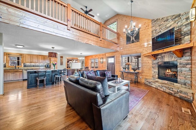 living room featuring sink, light wood-type flooring, ceiling fan with notable chandelier, high vaulted ceiling, and a stone fireplace