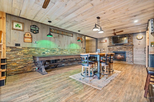 dining space with wooden walls, wooden ceiling, hardwood / wood-style floors, ceiling fan, and a stone fireplace