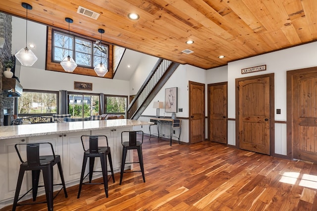 kitchen featuring wood finished floors, a kitchen bar, wooden ceiling, light stone countertops, and recessed lighting