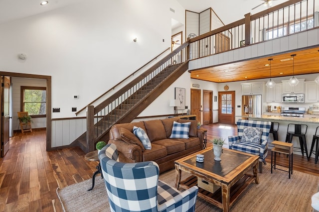 living room featuring a high ceiling, hardwood / wood-style floors, stairway, healthy amount of natural light, and wainscoting