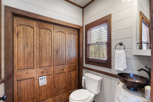 bathroom featuring a sink, toilet, washer / dryer, wooden walls, and ornamental molding
