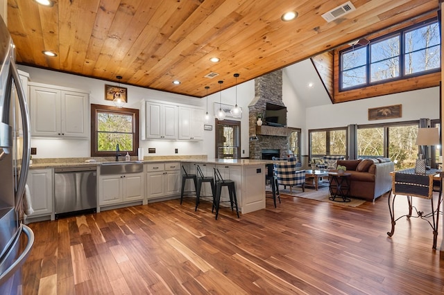 kitchen featuring stainless steel appliances, a peninsula, open floor plan, a stone fireplace, and wooden ceiling