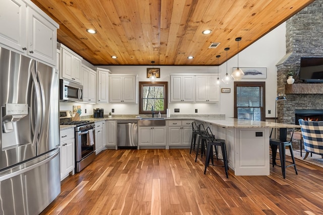 kitchen with stainless steel appliances, wooden ceiling, wood-type flooring, a peninsula, and a kitchen breakfast bar