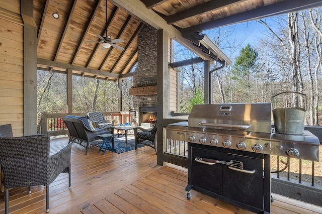 deck featuring a ceiling fan, an outdoor living space with a fireplace, and view of wooded area