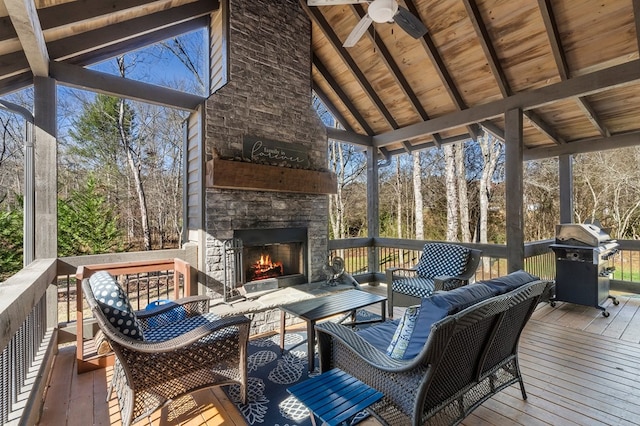 sunroom featuring an outdoor living space with a fireplace, ceiling fan, and view of wooded area
