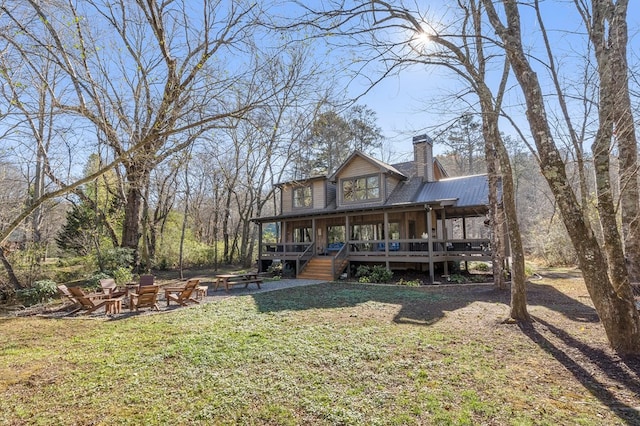 back of house featuring a fire pit, a chimney, a yard, metal roof, and a porch