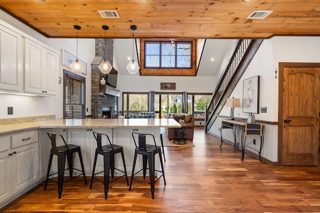 kitchen with wood ceiling, a stone fireplace, white cabinetry, wood finished floors, and open floor plan