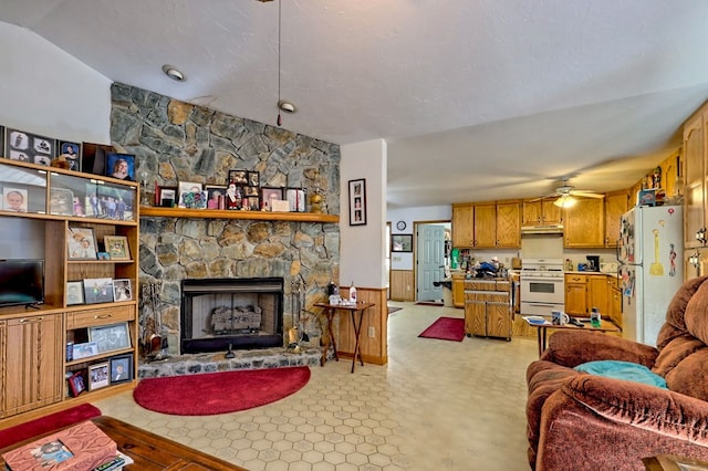 living room with ceiling fan, a stone fireplace, and lofted ceiling