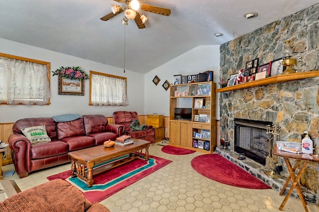 living room featuring ceiling fan, a stone fireplace, and lofted ceiling