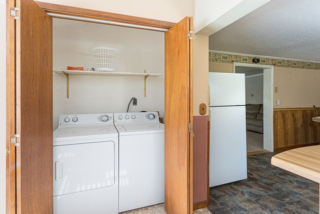 laundry area featuring a textured ceiling, washer and clothes dryer, ornamental molding, and wood walls