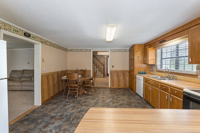 kitchen with white appliances, crown molding, sink, wooden walls, and a textured ceiling