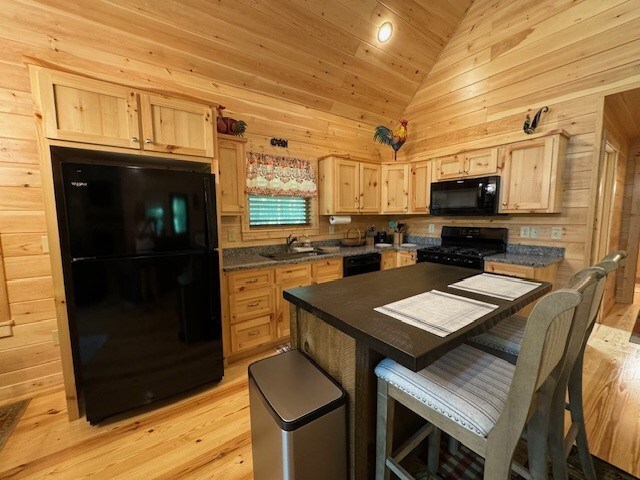 kitchen featuring light hardwood / wood-style flooring, light brown cabinetry, black appliances, wood walls, and sink