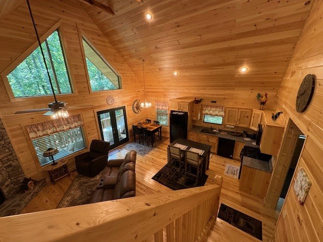 living room with ceiling fan with notable chandelier, high vaulted ceiling, light wood-type flooring, wood walls, and wooden ceiling